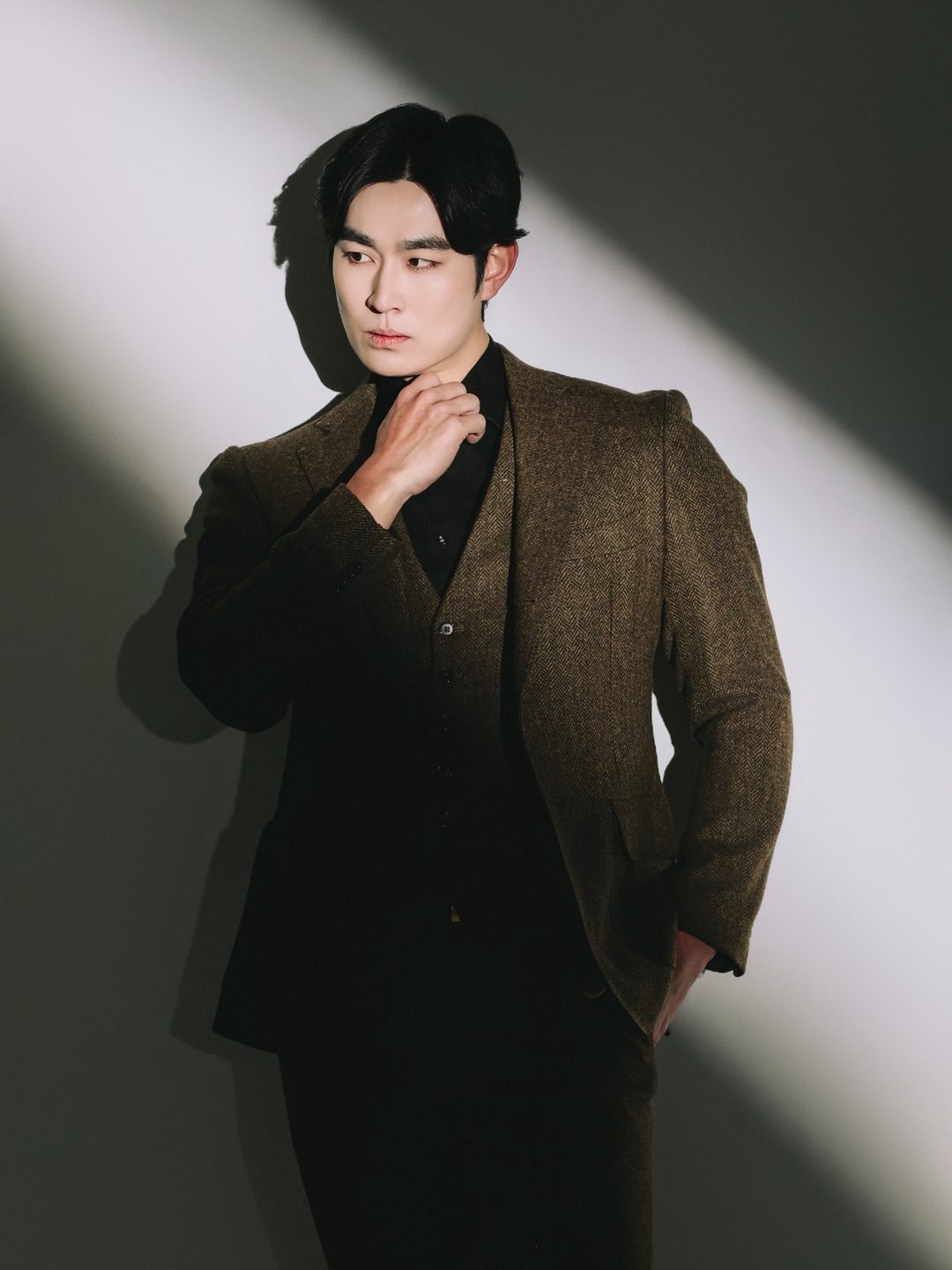 빛줄기 사이에서 턱을 괸 트위드 재킷 차림의 박기태